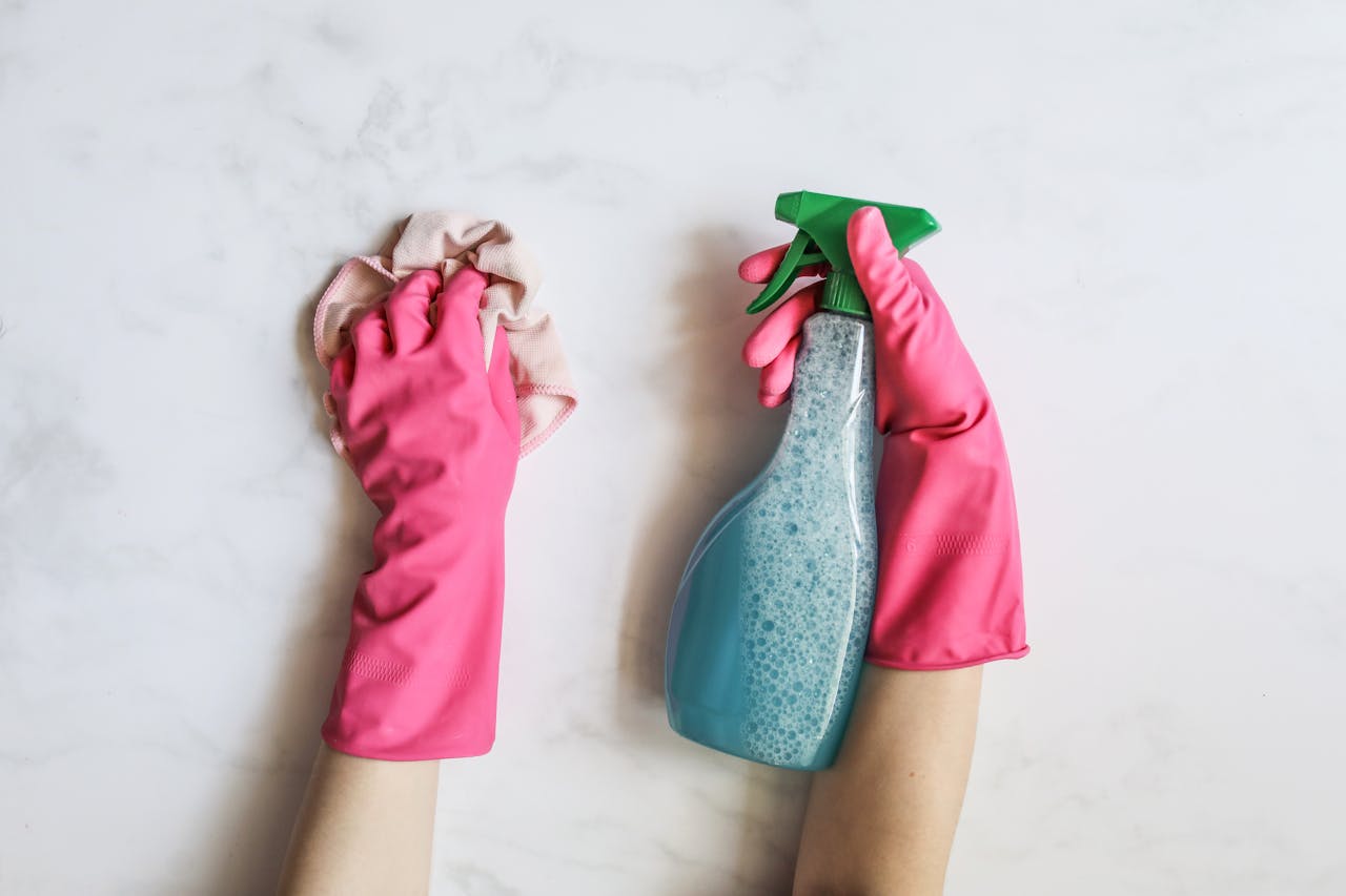 our-journey-03 A pair of hands in pink gloves are cleaning with a spray bottle on a white background.