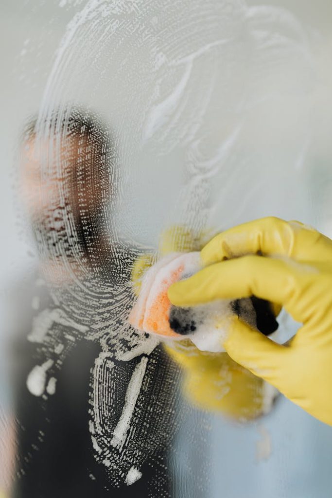 Mastering the First Impression: Your intriguing post title goes here A man wearing yellow gloves cleans a bathroom mirror with a soapy sponge, ensuring hygiene and cleanliness.
