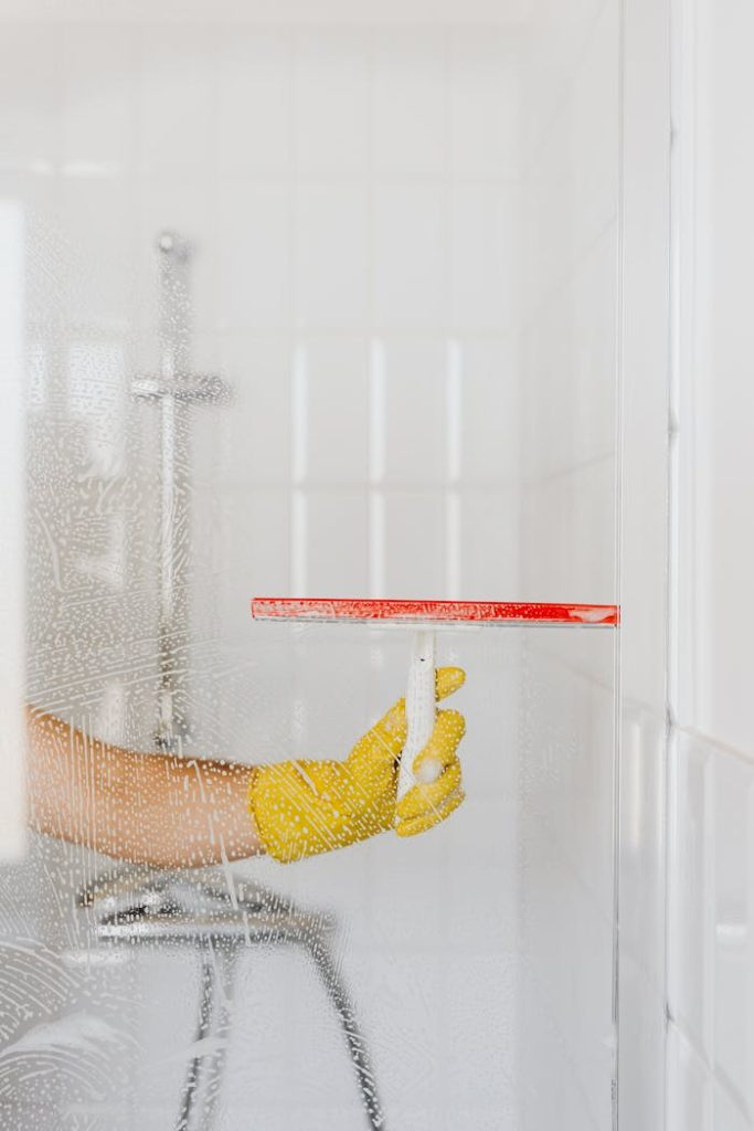 The Art of Drawing Readers In: Your attractive post title goes here A person wearing a yellow glove cleans a shower glass with a squeegee, emphasizing hygiene and cleanliness.