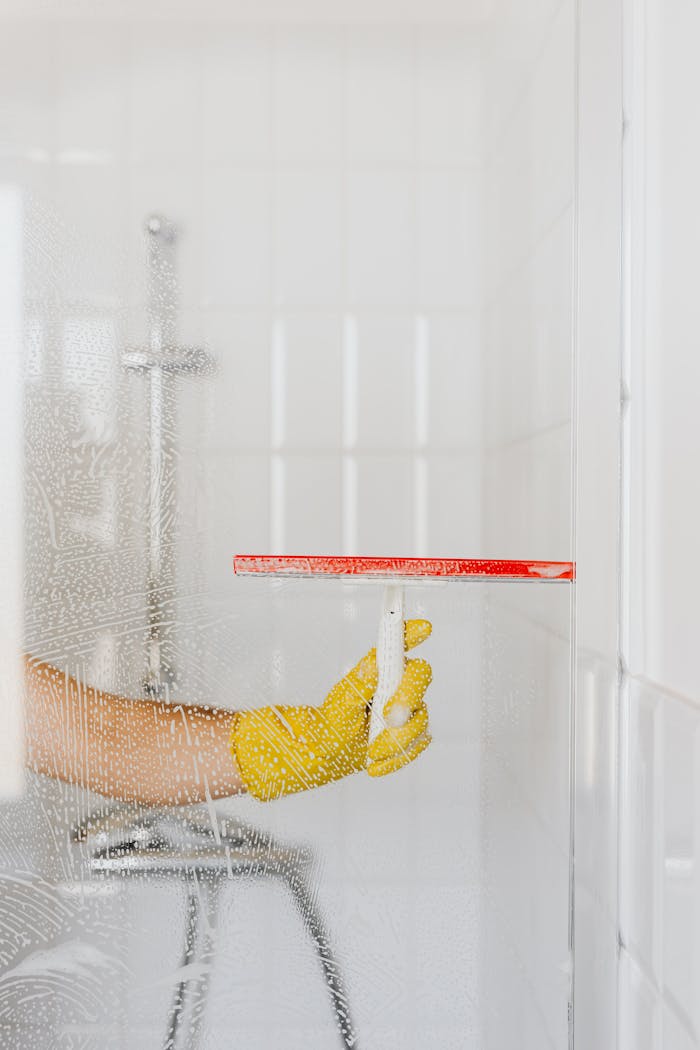 The Art of Drawing Readers In: Your attractive post title goes here A person wearing a yellow glove cleans a shower glass with a squeegee, emphasizing hygiene and cleanliness.