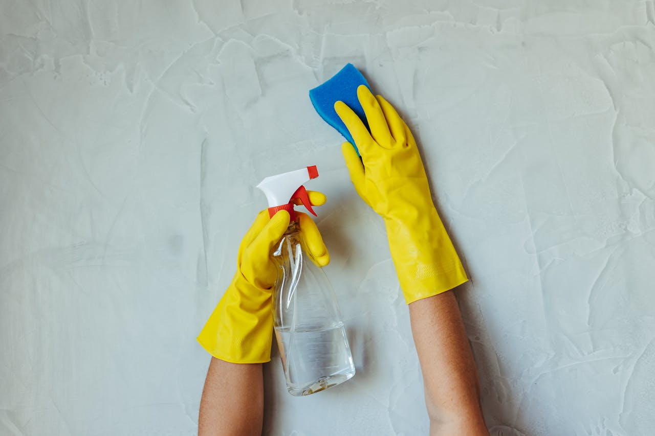 our-journey-02 Close-up of hands in yellow gloves cleaning a wall with a spray bottle and sponge.