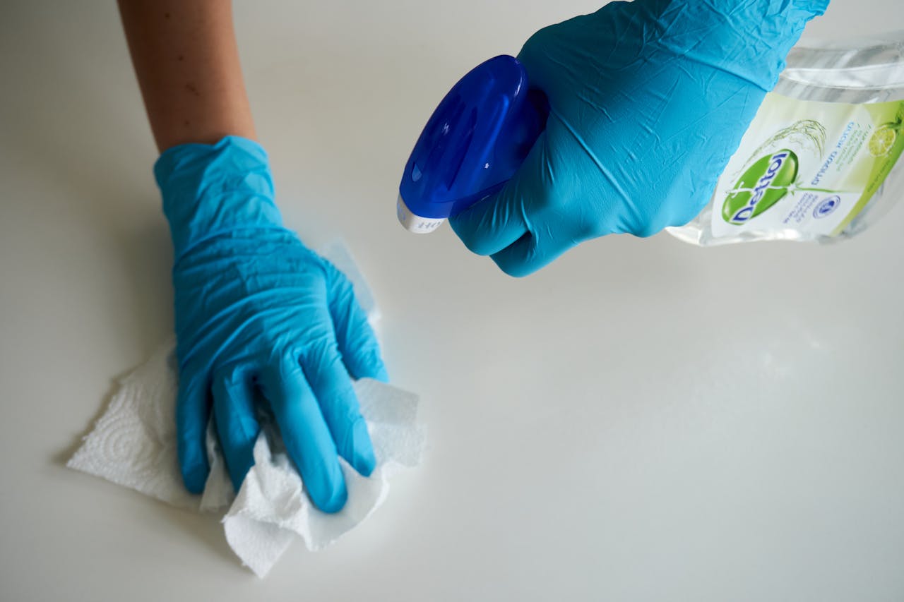 who-we-are Close-up of hands wearing gloves cleaning a surface with disinfectant spray.